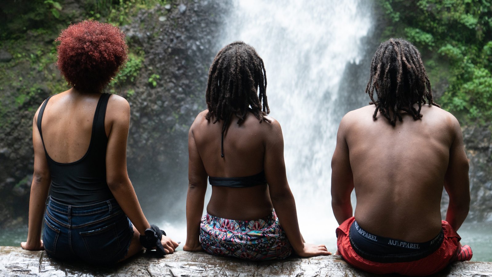 Trois personnes assises de dos face à une cascade, en pleine nature